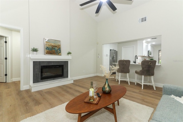 living room featuring a tiled fireplace, light wood-type flooring, sink, and high vaulted ceiling