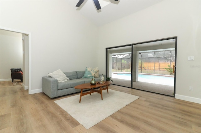 living room featuring ceiling fan, a towering ceiling, and light wood-type flooring