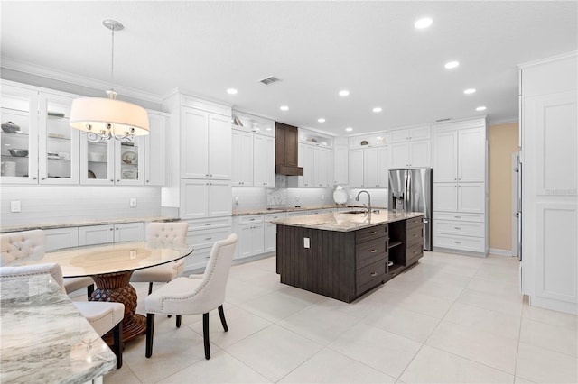 kitchen featuring hanging light fixtures, ornamental molding, a kitchen island with sink, dark brown cabinetry, and stainless steel refrigerator with ice dispenser