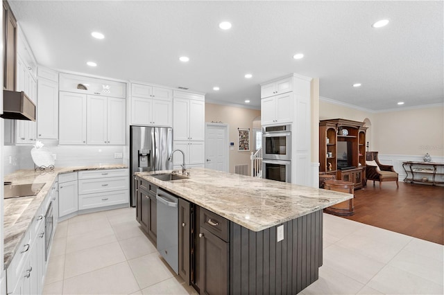 kitchen with appliances with stainless steel finishes, white cabinetry, sink, ornamental molding, and a center island with sink