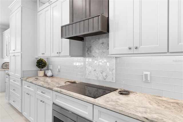 kitchen featuring backsplash, light stone counters, custom range hood, white cabinets, and black electric cooktop