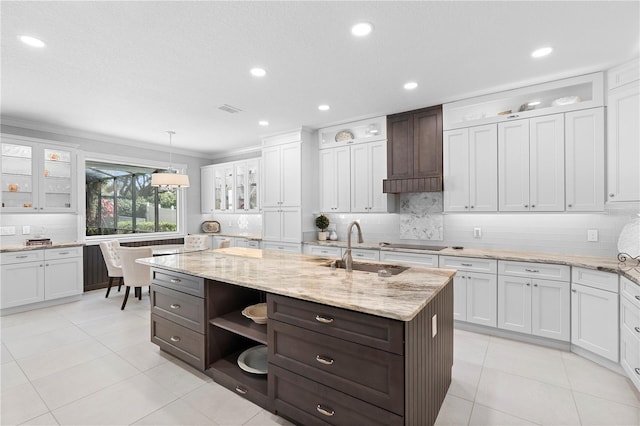 kitchen with white cabinetry, sink, backsplash, hanging light fixtures, and a center island with sink