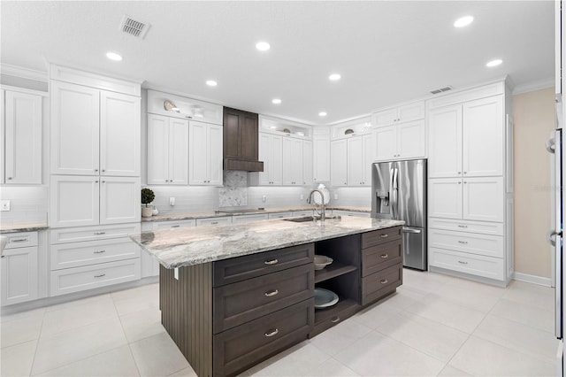 kitchen featuring white cabinetry, an island with sink, stainless steel fridge, and sink