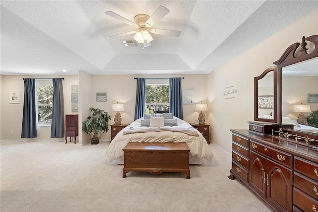 bedroom with ceiling fan, a raised ceiling, light carpet, and a textured ceiling