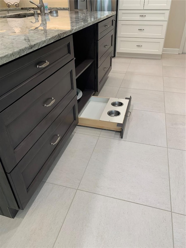 interior space featuring sink, light tile patterned floors, white cabinets, and light stone counters