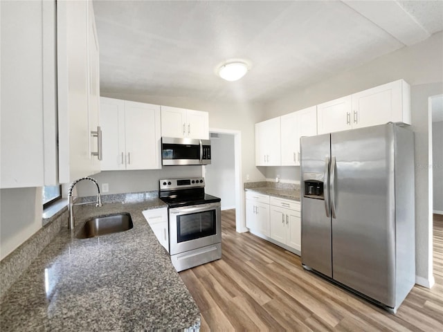 kitchen featuring white cabinetry, sink, dark stone countertops, light hardwood / wood-style flooring, and stainless steel appliances