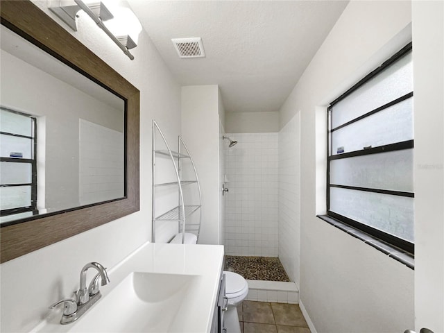 bathroom with tile patterned floors, tiled shower, toilet, a textured ceiling, and vanity