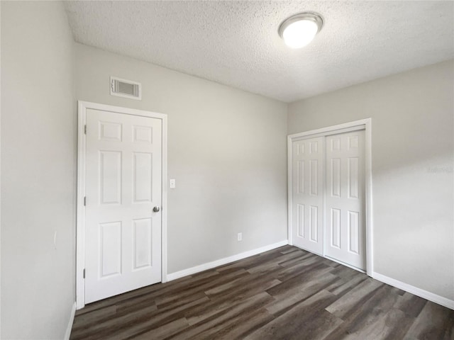 unfurnished bedroom featuring a textured ceiling, dark hardwood / wood-style floors, and a closet