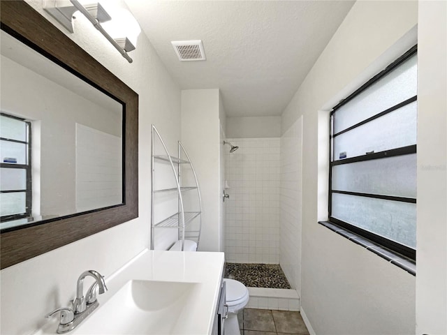 bathroom with toilet, a textured ceiling, tile patterned flooring, tiled shower, and vanity