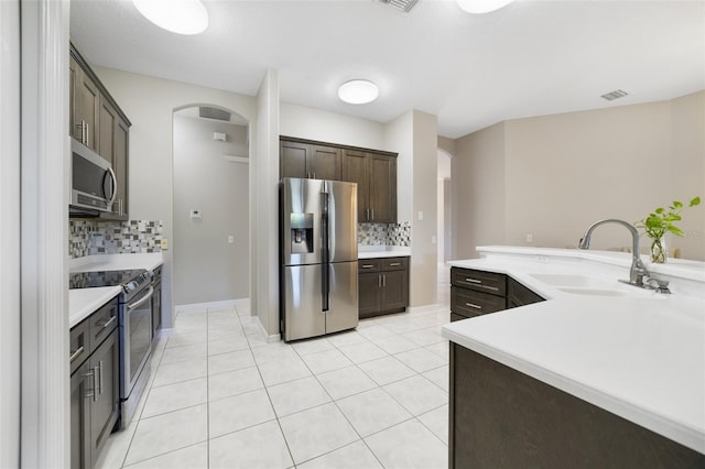 kitchen with appliances with stainless steel finishes, tasteful backsplash, sink, light tile patterned floors, and dark brown cabinets