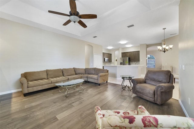 living room featuring dark hardwood / wood-style flooring, ceiling fan with notable chandelier, and a tray ceiling