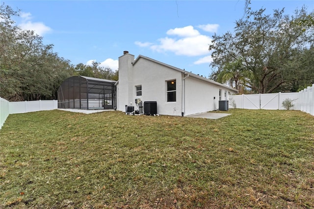 rear view of house featuring cooling unit, a yard, a patio area, and glass enclosure