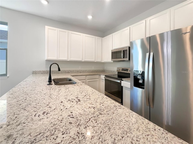 kitchen featuring white cabinets, appliances with stainless steel finishes, sink, and light stone counters