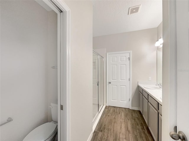 bathroom with toilet, vanity, wood-type flooring, a textured ceiling, and a shower with door