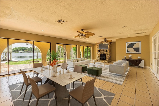 tiled dining area with ceiling fan, a water view, a wealth of natural light, and a fireplace