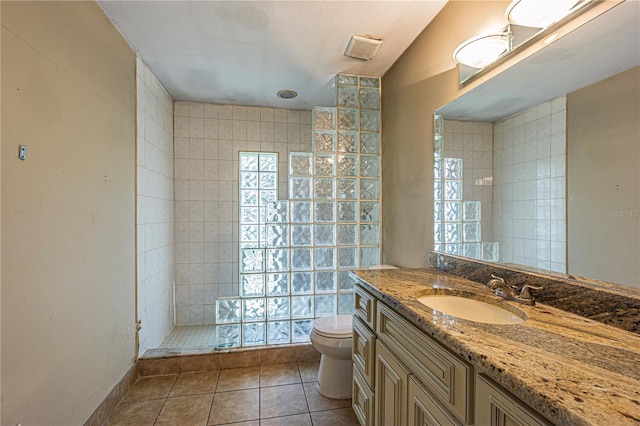 bathroom featuring tile patterned floors, toilet, vanity, and a tile shower