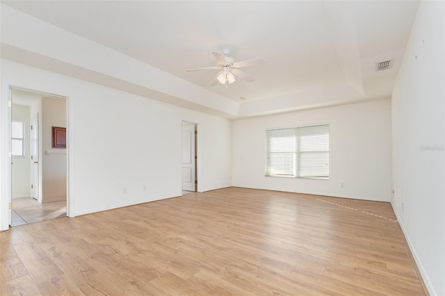 spare room featuring a tray ceiling, light wood-style floors, visible vents, and ceiling fan