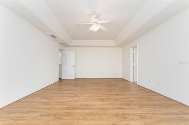 empty room with ceiling fan, a raised ceiling, and light hardwood / wood-style floors