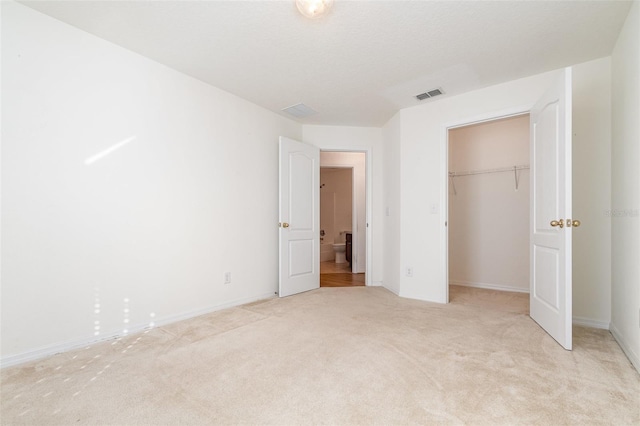 unfurnished bedroom with a closet, a spacious closet, light carpet, and a textured ceiling