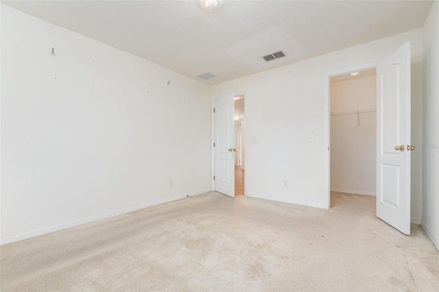 unfurnished bedroom with a walk in closet, light carpet, and a closet