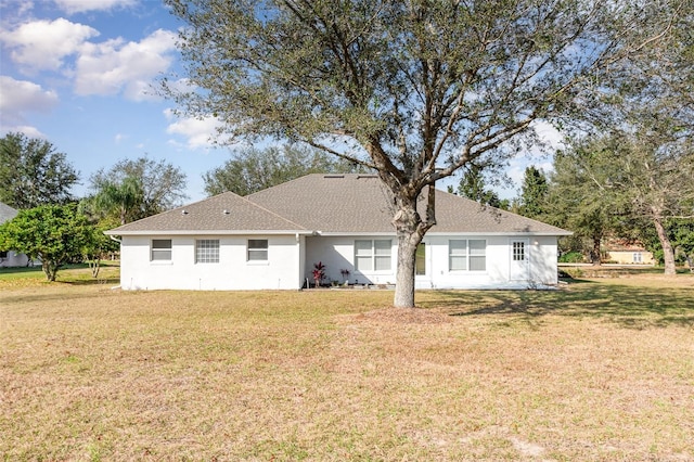 rear view of property featuring a lawn, a shingled roof, and stucco siding