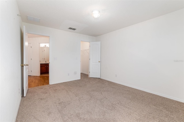 unfurnished bedroom with visible vents, a walk in closet, baseboards, carpet, and a closet