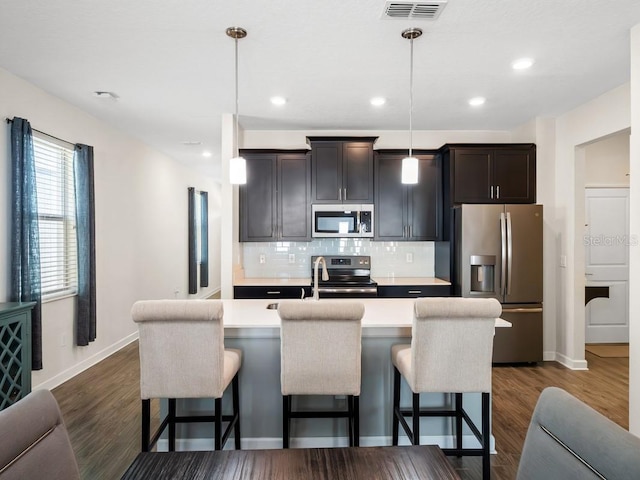 kitchen featuring pendant lighting, a breakfast bar, backsplash, stainless steel appliances, and a center island with sink