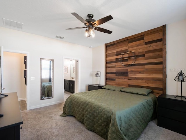 bedroom with ceiling fan, carpet flooring, connected bathroom, and wooden walls