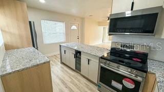 kitchen with light wood-type flooring, light stone countertops, appliances with stainless steel finishes, and white cabinets