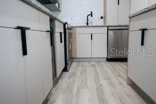 kitchen with white cabinets, freestanding refrigerator, light countertops, light wood-style floors, and stainless steel dishwasher