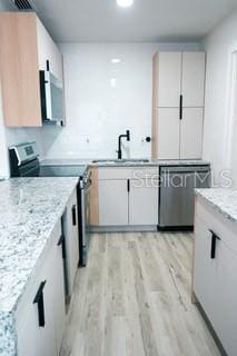 kitchen featuring light stone counters, a sink, white cabinetry, appliances with stainless steel finishes, and light wood finished floors