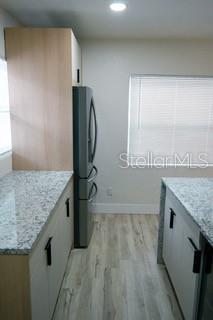 kitchen featuring light stone counters, freestanding refrigerator, light wood-type flooring, and baseboards