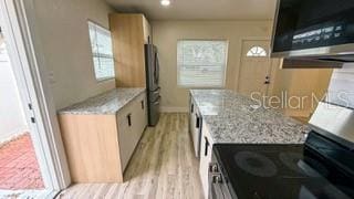 kitchen featuring stainless steel appliances, baseboards, light stone counters, and light wood finished floors