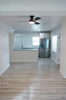 unfurnished living room featuring light wood-style flooring, baseboards, and a ceiling fan