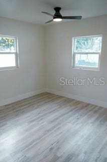 empty room with light wood finished floors, a ceiling fan, and baseboards