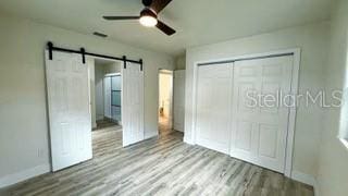 unfurnished bedroom with a barn door, a ceiling fan, baseboards, light wood-style floors, and a closet