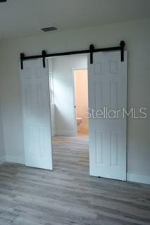 interior space featuring a barn door, wood finished floors, visible vents, and baseboards