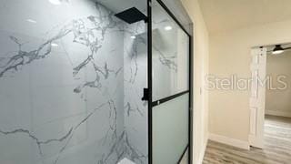 bathroom with a marble finish shower, baseboards, and wood finished floors