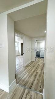 corridor featuring vaulted ceiling, light wood-style flooring, and baseboards