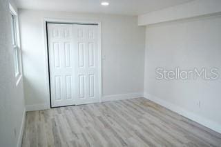 unfurnished bedroom with light wood-type flooring, a closet, baseboards, and recessed lighting