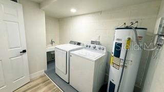 clothes washing area featuring laundry area, water heater, separate washer and dryer, and light wood finished floors