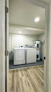 laundry room with laundry area, washing machine and dryer, electric water heater, and light wood-style floors