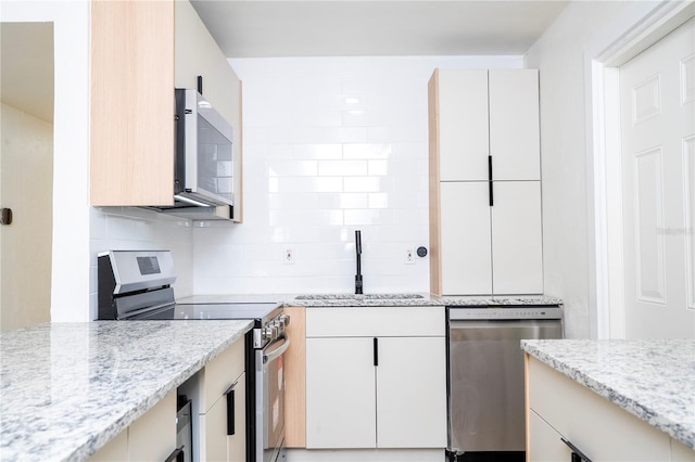 2002 Geigel Ave, Orlando, FL 32806 - kitchen with light stone countertops, a sink, white cabinetry, decorative backsplash, and appliances with stainless steel finishes