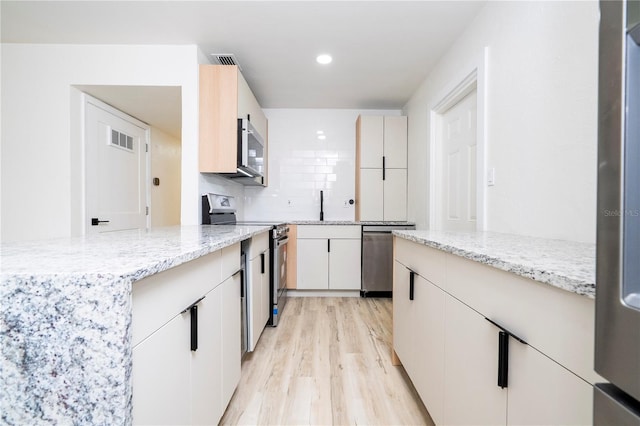2002 Geigel Ave, Orlando, FL 32806 - kitchen featuring appliances with stainless steel finishes, visible vents, light stone countertops, and light wood-type flooring