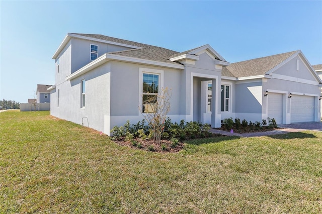 view of front of house with roof with shingles, a front yard, an attached garage, and stucco siding