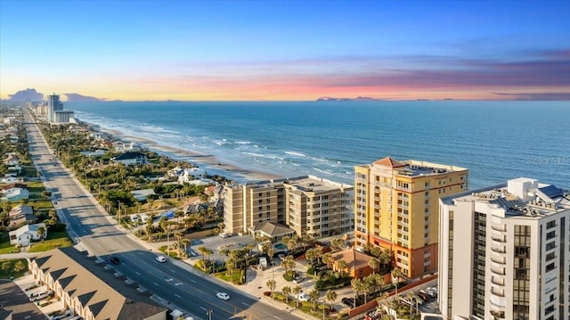 aerial view at dusk featuring a water view and a beach view