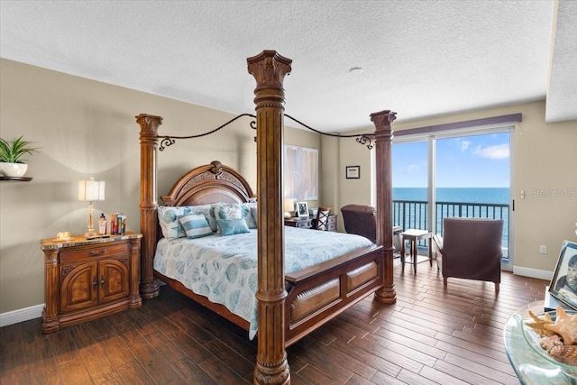 bedroom featuring dark hardwood / wood-style flooring, access to exterior, a textured ceiling, and a water view