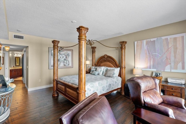 bedroom with dark hardwood / wood-style flooring, connected bathroom, decorative columns, and a textured ceiling