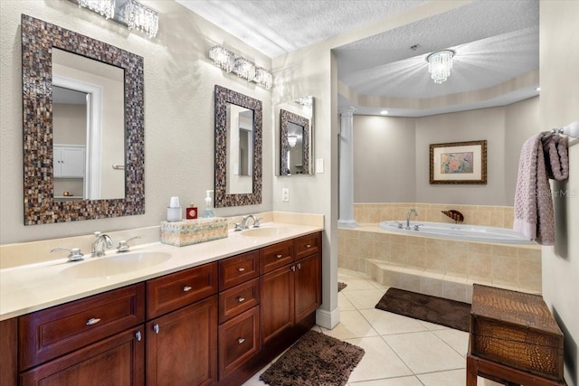 bathroom featuring tile patterned floors, ornate columns, a textured ceiling, vanity, and tiled tub