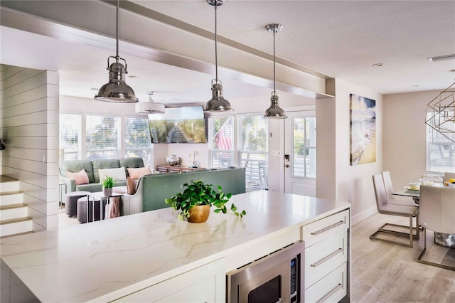 kitchen featuring white cabinetry, decorative light fixtures, stainless steel microwave, and light stone countertops